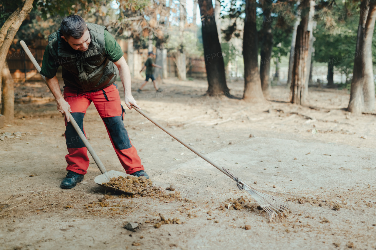 Caretaker with down syndrome in the cleaning animal enclosure. Concept of integration people with disabilities into society.