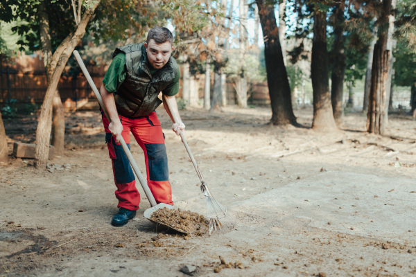 Caretaker with down syndrome in the cleaning animal enclosure. Concept of integration people with disabilities into society.