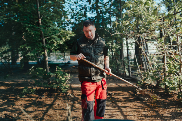 Caretaker with down syndrome in the cleaning animal enclosure. Concept of integration people with disabilities into society.