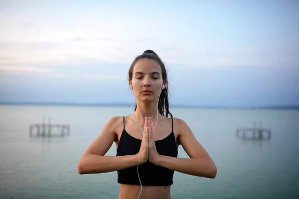 A young beautiful sportive girl meditating at early morning by the lake.