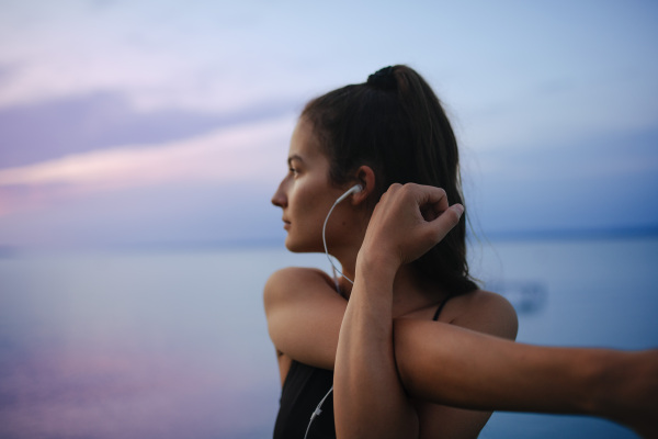 Young sportive girl stretching in the morning and listening music, outdoor near sea.