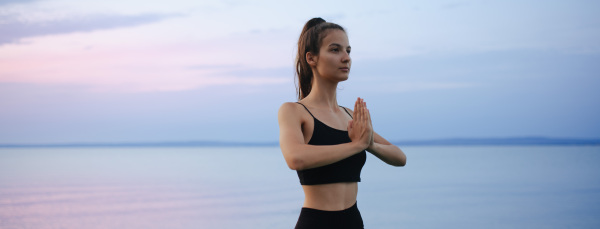 A young beautiful sportive girl meditating at early morning by the lake.