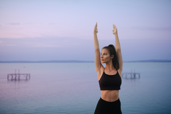 A young beautiful sportive girl meditating at early morning by the lake.