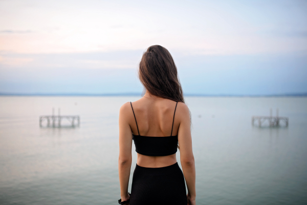 A rear view of young beautiful sportive girl standing by the lake on early morning and contamplating.