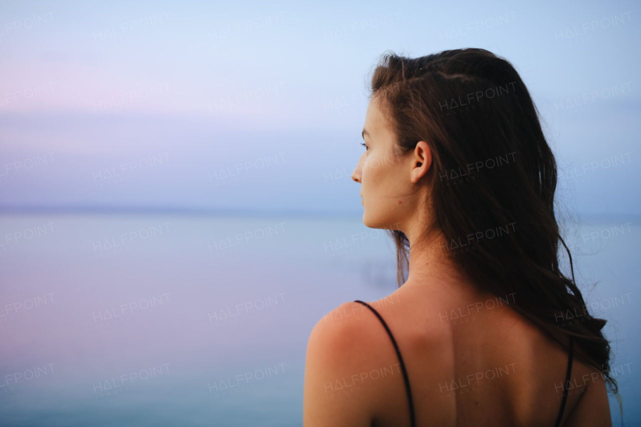 A rear view of young beautiful sportive girl standing by the lake on early morning and contamplating.