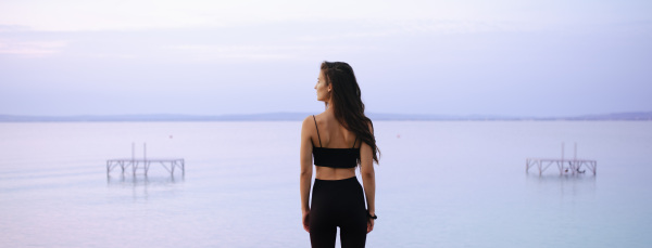 A rear view of young beautiful sportive girl standing by the lake on early morning and contamplating.