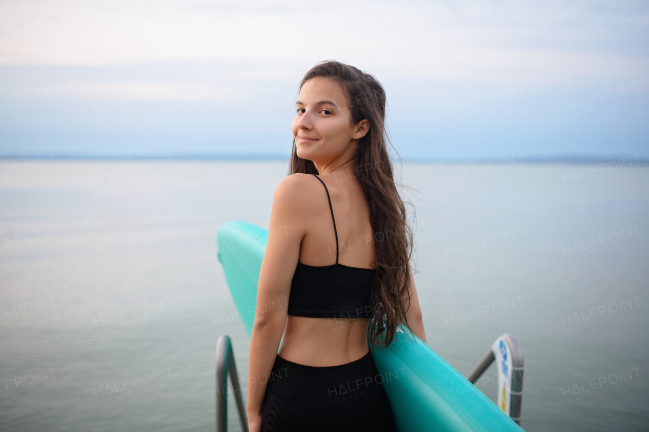 A young beautiful sportive girl with paddleboard on the lake at sunrise