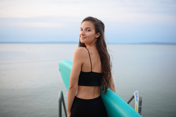 A young beautiful sportive girl with paddleboard on the lake at sunrise