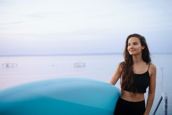 A young beautiful sportive girl with paddleboard on the lake at sunrise