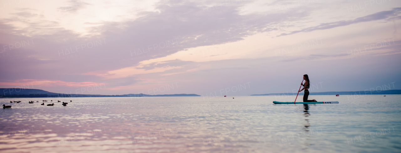 A young beautiful girl surfer paddling on surfboard on the lake at sunrise