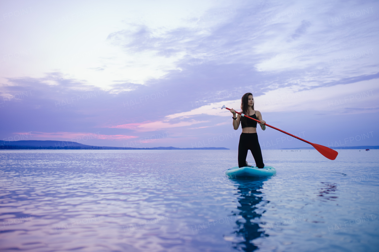 A young beautiful girl surfer paddling on surfboard on the lake at sunrise