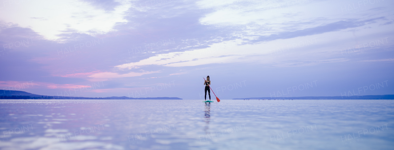 A young beautiful girl surfer paddling on surfboard on the lake at sunrise