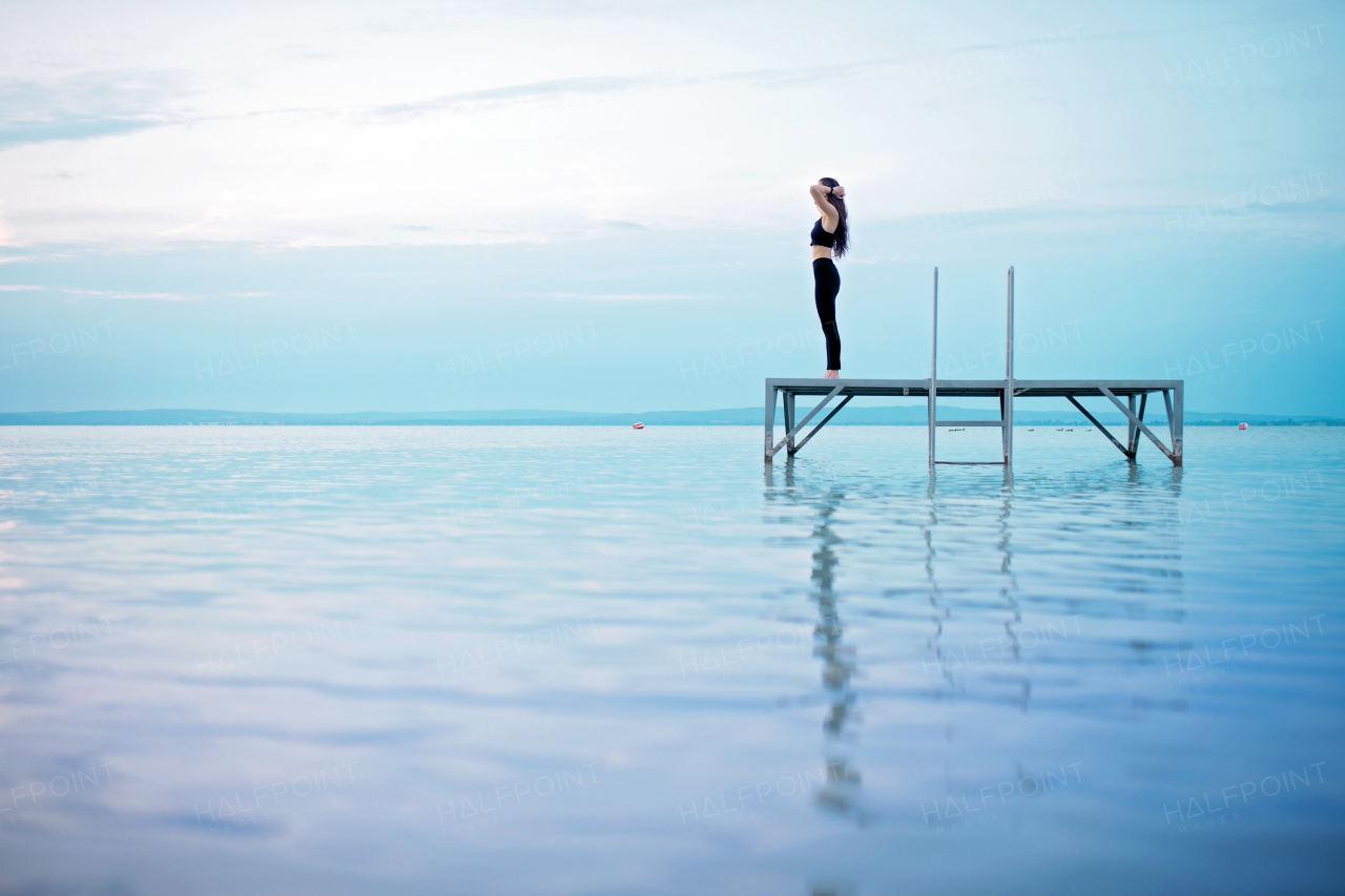 A young beautiful sportive girl meditating at early morning by the lake.