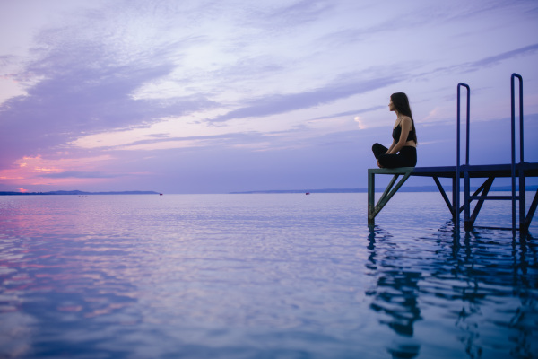 A young beautiful sportive girl meditating at early morning by the lake.