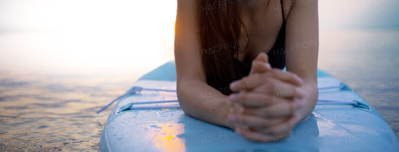 A young surfer girl lying on surfboard and meditating on the lake at sunrise, cut out