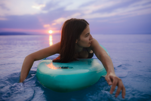 A young beautiful girl surfer paddling on surfboard on the lake at sunrise