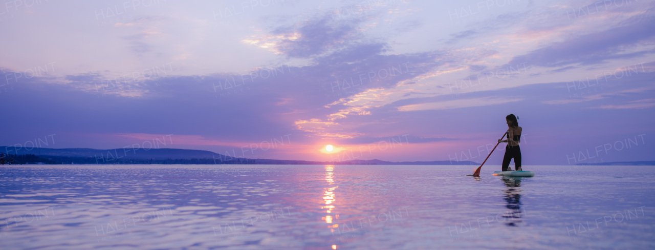 A young beautiful girl surfer paddling on surfboard on the lake at sunrise