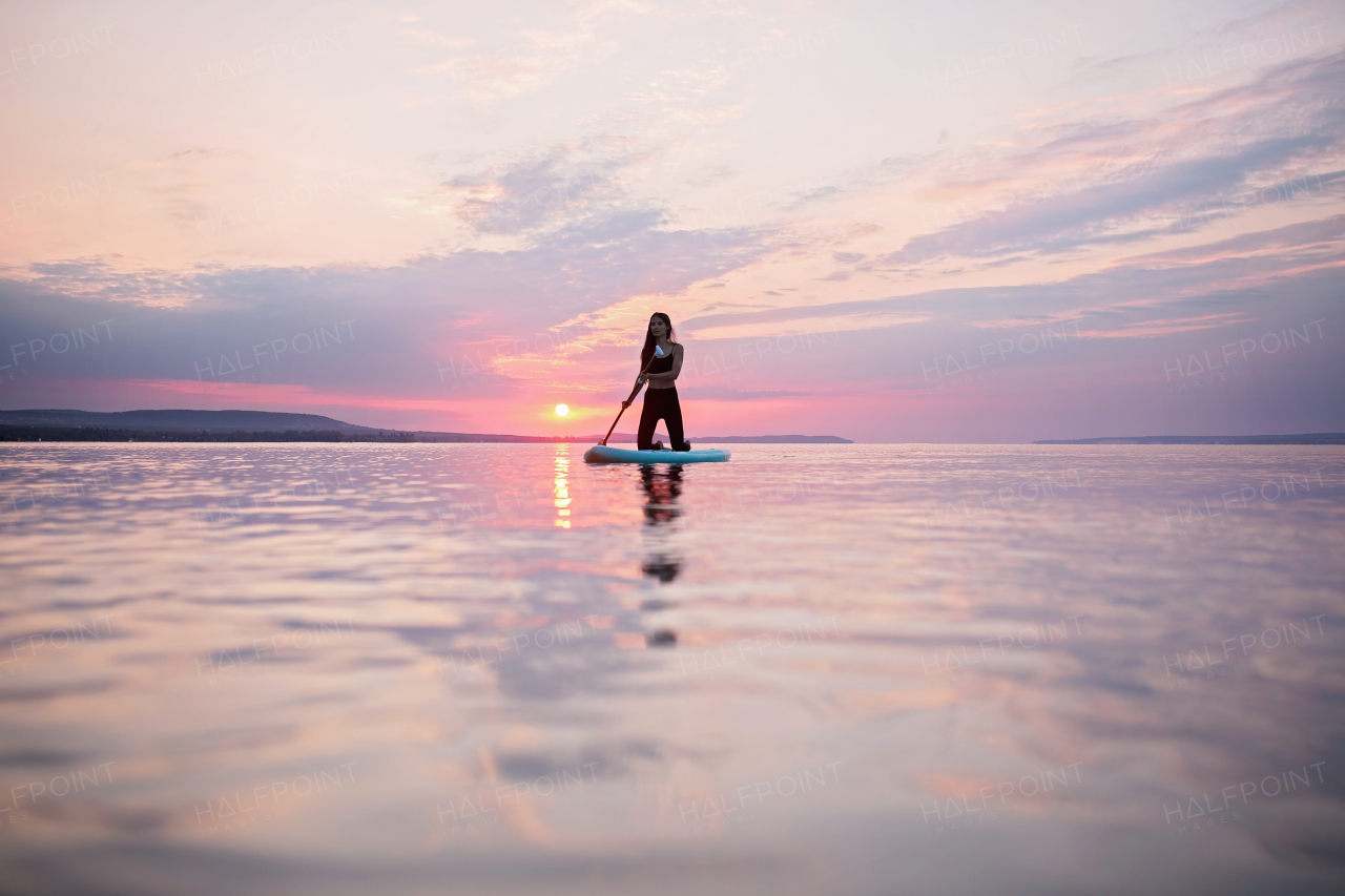 A young beautiful girl surfer paddling on surfboard on the lake at sunrise