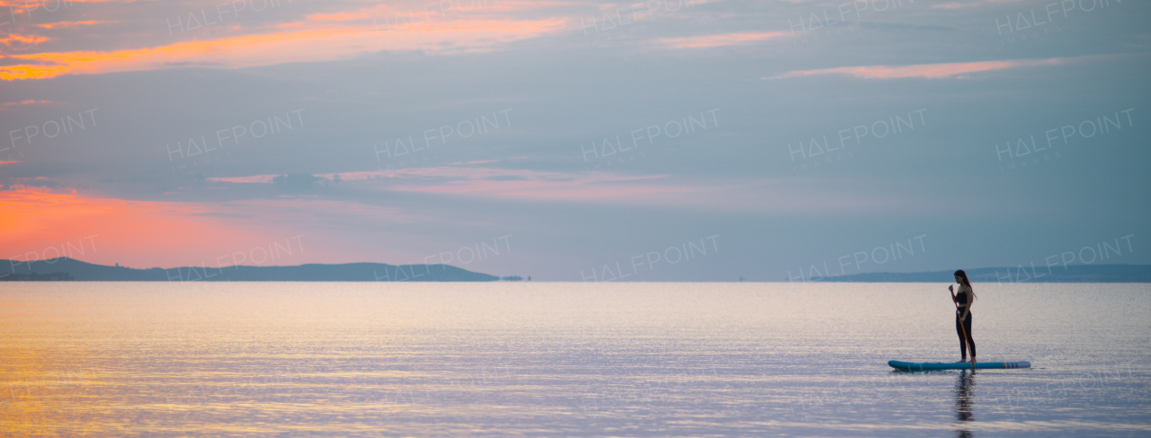 A young surfer girl paddling on surfboard on the lake at sunrise