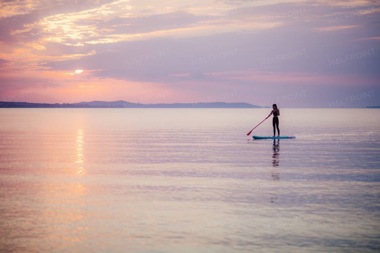 A young beautiful girl surfer paddling on surfboard on the lake at sunrise