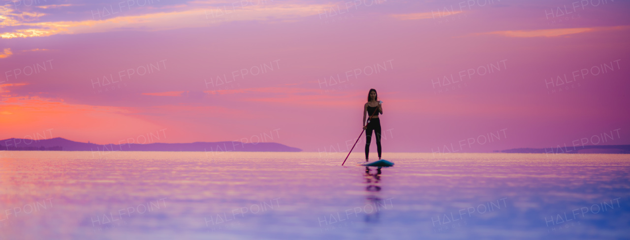 A young beautiful girl surfer paddling on surfboard on the lake at sunrise