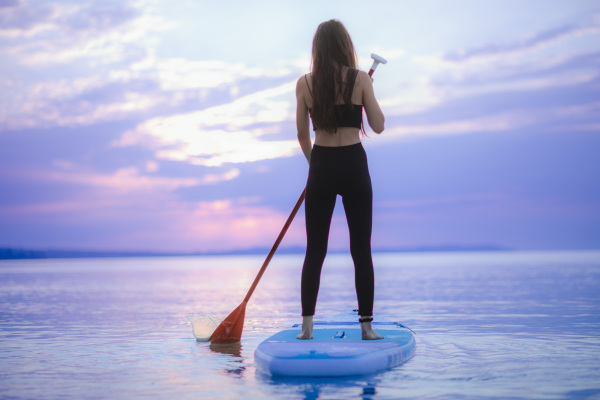 A young girl surfer paddling on surfboard on the lake at sunrise.