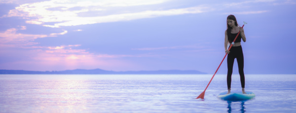 A young beautiful girl surfer paddling on surfboard on the lake at sunrise