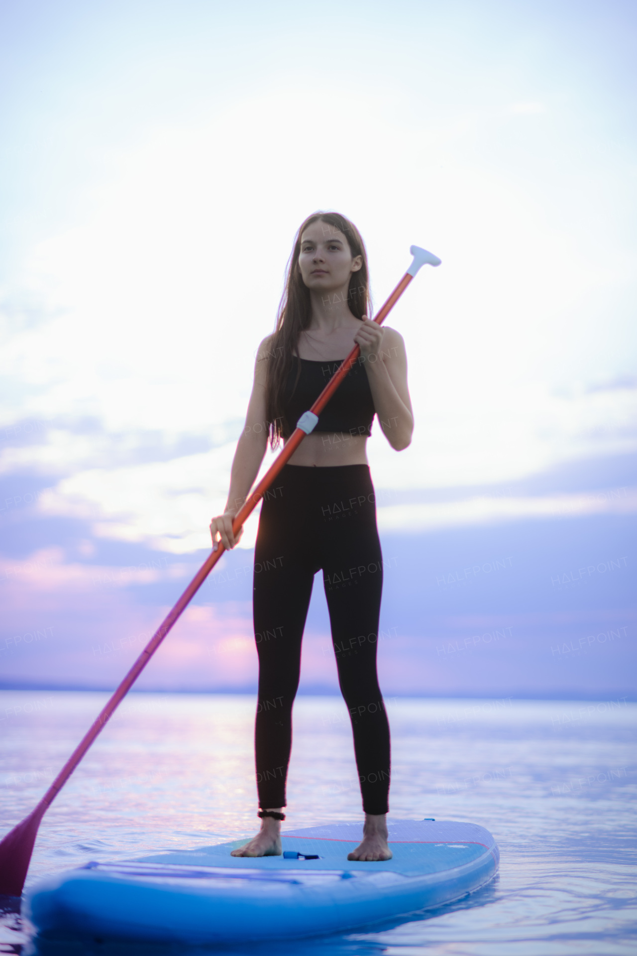 A young beautiful girl surfer paddling on surfboard on the lake at sunrise