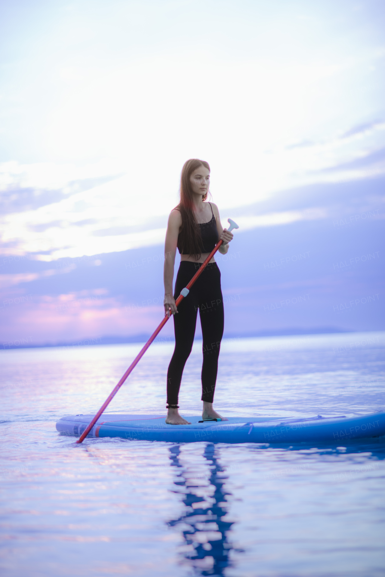 A young beautiful girl surfer paddling on surfboard on the lake at sunrise