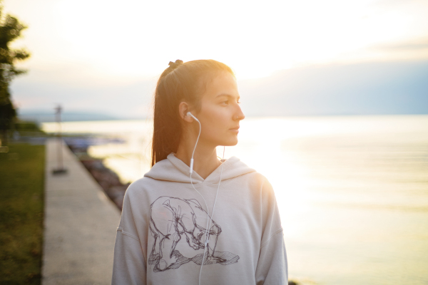 A young beautiful sportive girl listening to music at sunrise by the lake.