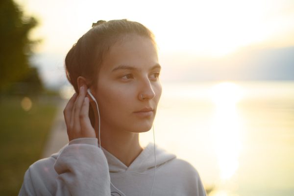 A young beautiful sportive girl listening to music at sunrise by the lake.