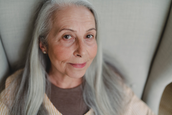 A close up of senior woman sitting in armchair and looking at camera.