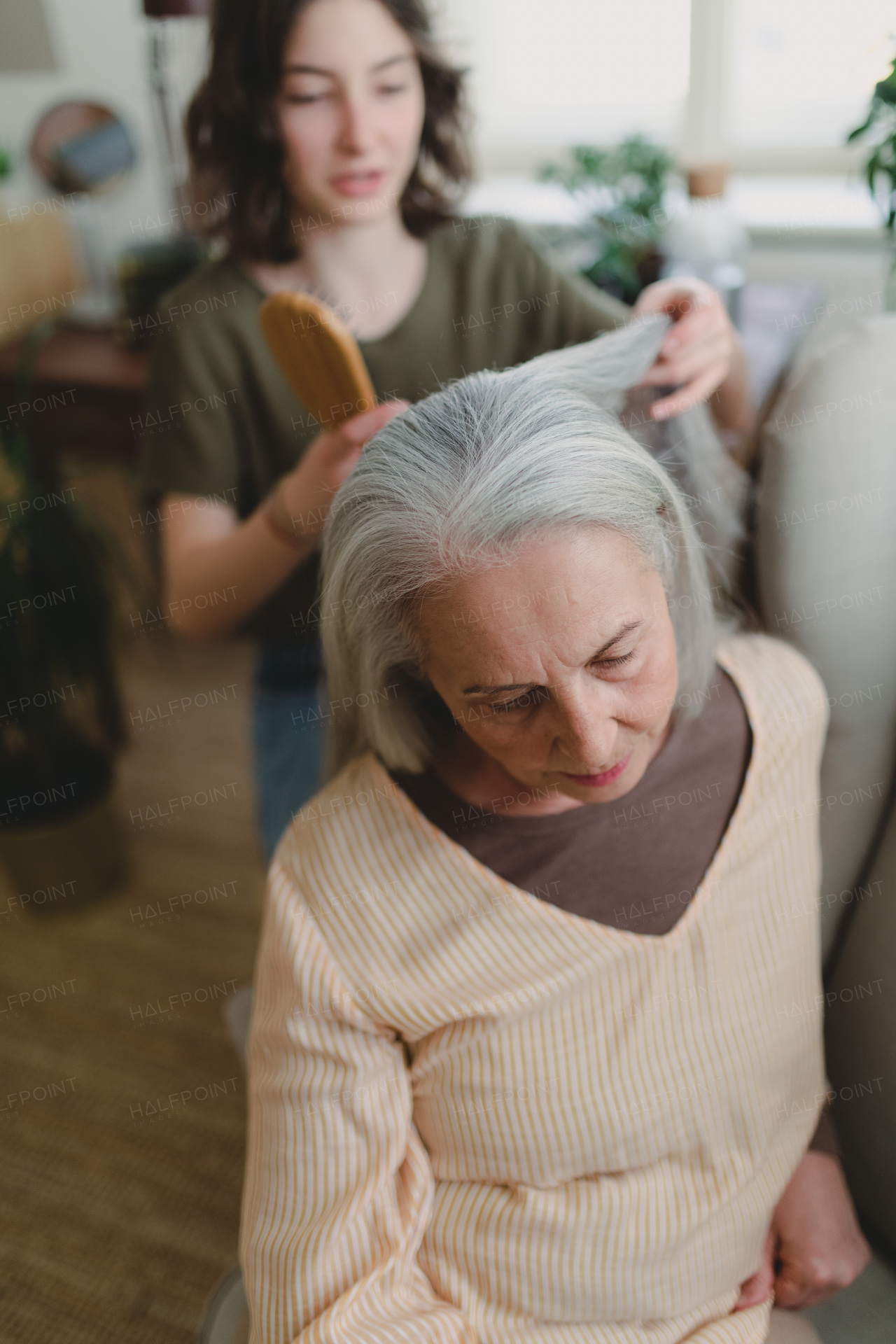 A teenage girl brushing her grandmother's hair at home.