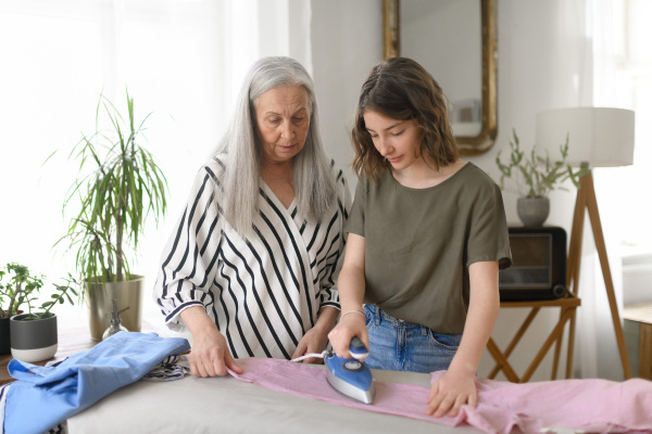 A teenage girl ironing and helping with household chores her senior grandmother at home