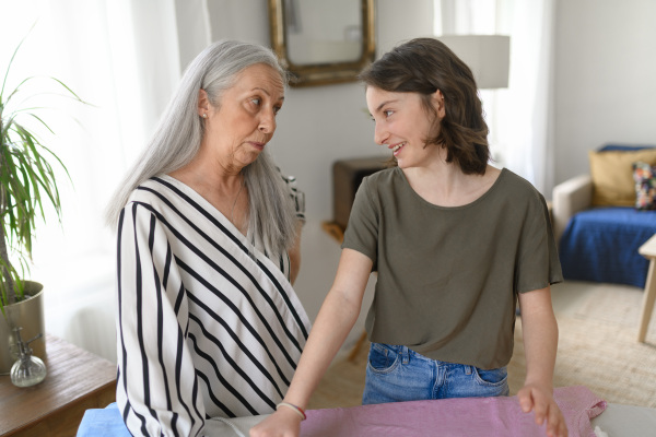 A teenage girl ironing and helping with household chores her senior grandmother at home