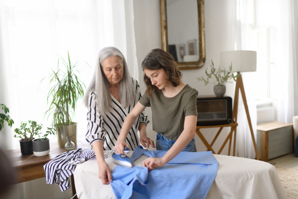 A teenage girl ironing and helping with household chores her senior grandmother at home