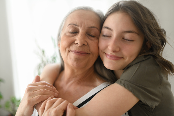 A senior grandmother with teenage granddaguhter hugging together at home.