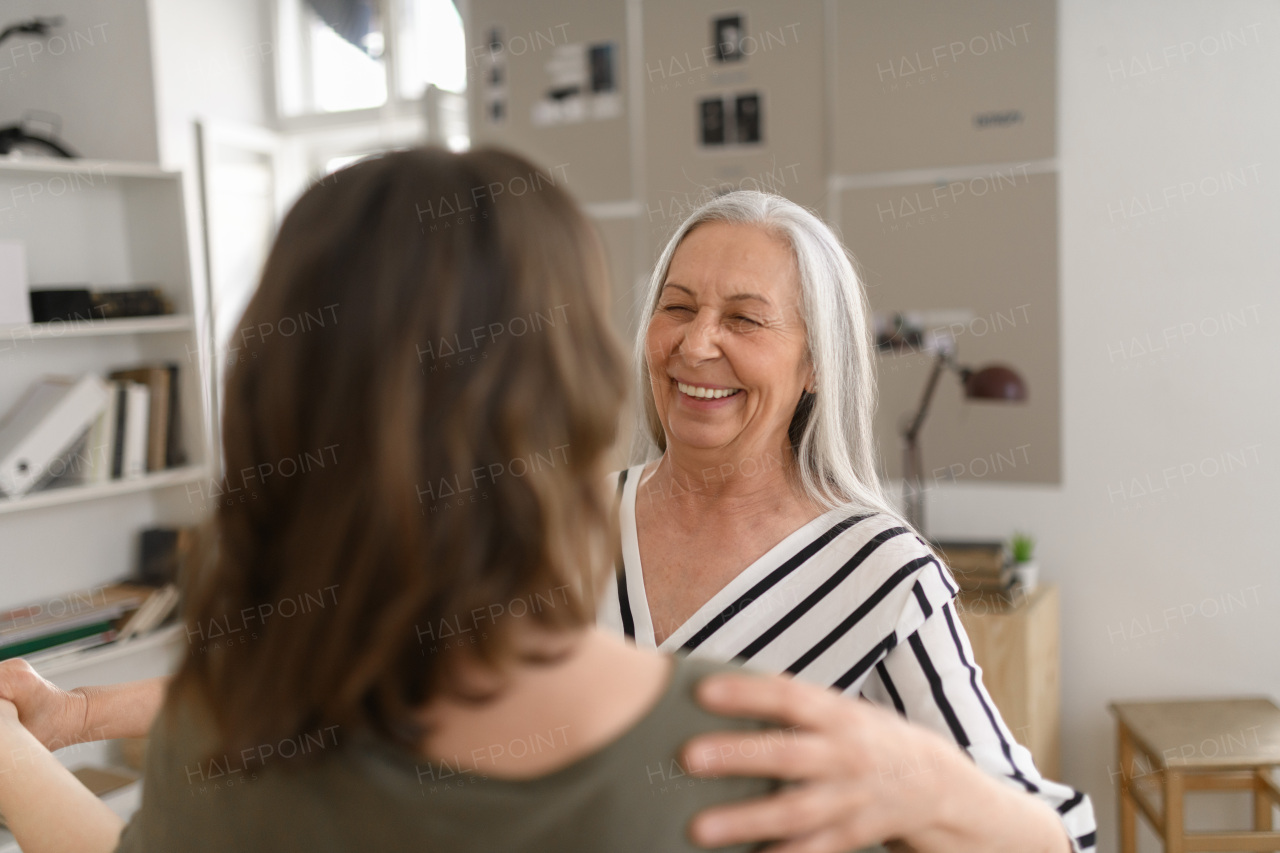 A happy senior grandmother with teenage granddaguhter dancing together at home.