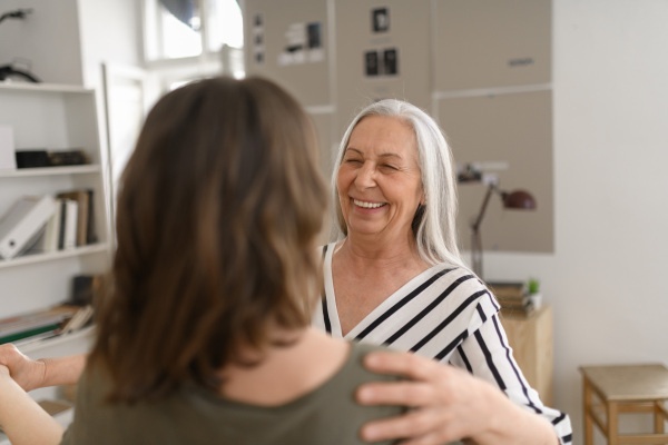 A happy senior grandmother with teenage granddaguhter dancing together at home.