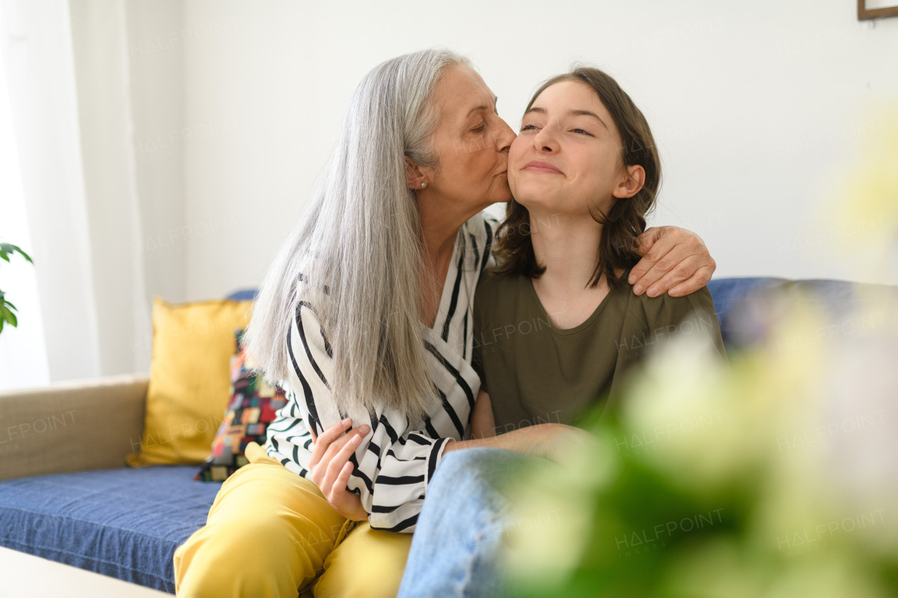 A senior grandmother with teenage granddaguhter having good time together at home, hugging and kissing on cheeck.