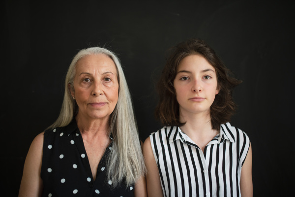 A portrait of senior grandmother with her granddaughter looking at camera over black blackground