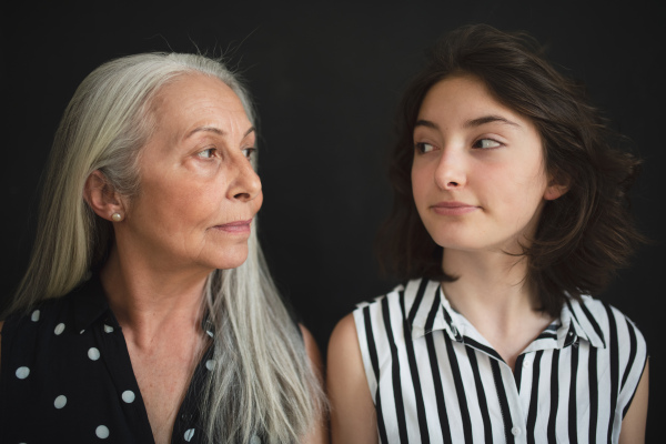 A portrait of senior grandmother with her granddaughter looking at each other over black blackground