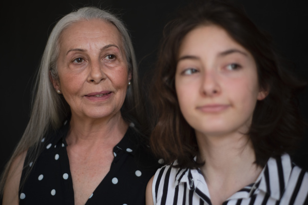 A portrait of senior grandmother with her granddaughter looking at camera over black blackground