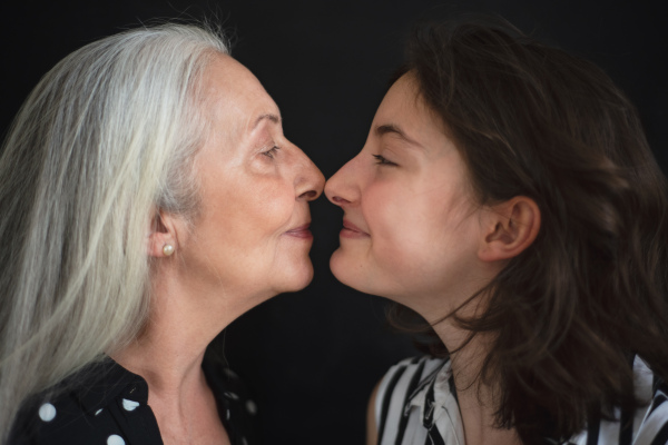 A portrait of senior grandmother with her granddaughter looking at each other face to face, over black blackground