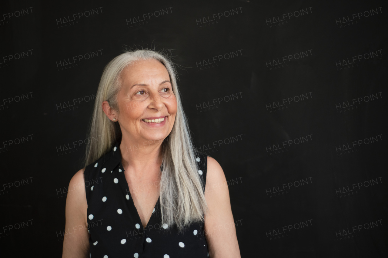 A portrait of cheerful senior woman with long grey hair over black background.