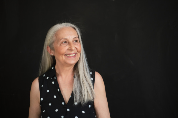 A portrait of cheerful senior woman with long grey hair over black background.