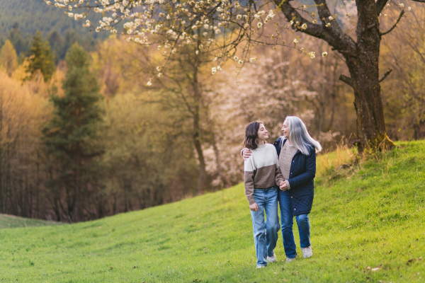 A happy senior grandmother with teenage granddaguhter on walk in nature on spring day.