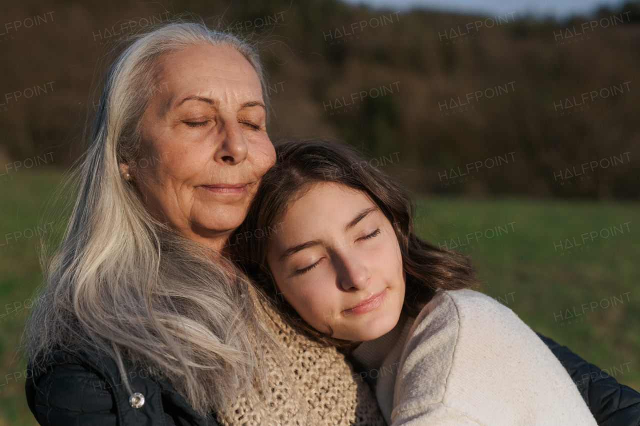 A happy senior grandmother with teenage granddaguhter hugging in nature on spring day.