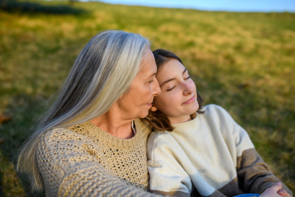 A happy senior grandmother with teenage granddaguhter hugging in nature on spring day.