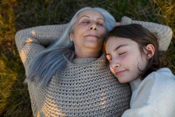 A happy senior grandmother with teenage granddaguhter hugging in nature on spring day.